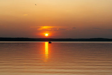 the sun sets over the horizon. A boat is floating in the sea.