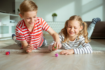 Portrait of two cheerful children laying on the floor and playing with colorful dices