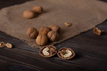 two halves of a walnut lie on a wooden table in the foreground. Whole walnuts lie on linen cloth. peeled nuts and shell fragments lie around