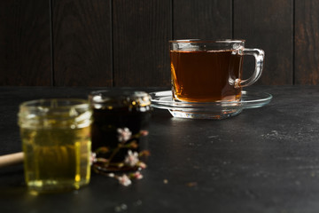 Cup of black tea in focus and two type of honey on foreground with dark background