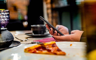Obraz na płótnie Canvas woman hand using mobile phone in cafe with a piece of pizza in plate on table