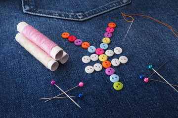 Fototapeta na wymiar Sewing and repair of clothes. The yen mark is laid out with buttons on jeans. Thimble, needle, thread, pins