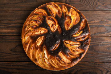 failed apple pie. burnt on top and the dough did not rise during baking. textured burnt pie crust. lies on a wooden table. view from above