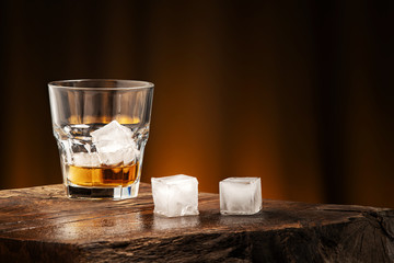 A glass of alcoholic beverage on a wooden table. Whiskey cocktail with ice
