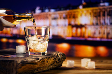 Pouring whiskey into a glass with ice against the background of the night city. A glass of...