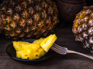 Sliced pineapple on old rustic desk with knife and with whole pineapple behind. Black background.