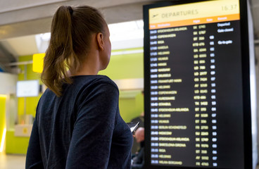 Woman in front of flight information board, checking her flight.