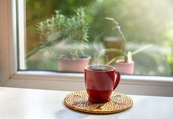 Red cup with fresh black coffee placed by the window