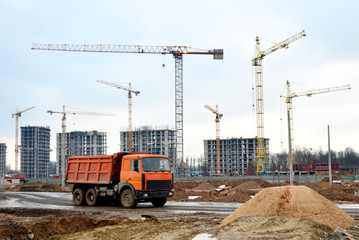 Dump truck on the construction site against tower cranes and constructing a new residential building. Renovation program, development, concept of the buildings industry.