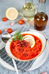 Ukrainian vegetarian borscht with red beans in a white plate stands on a gray concrete background.