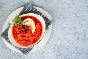 Ukrainian vegetarian borscht with red beans in a white plate stands on a gray concrete background. Top view