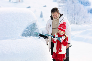 Father and child brushing off car in winter.