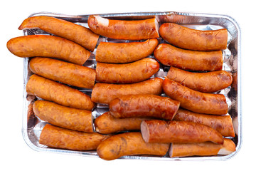 The seasoned and incised sausage lying on an aluminum tray, isolated on a white background with a clipping path.