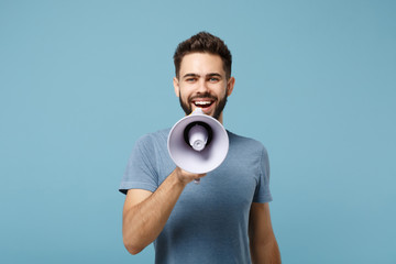 Young smiling attractive man in casual clothes posing isolated on blue wall background, studio portrait. People sincere emotions lifestyle concept. Mock up copy space. Holding, Scream in megaphone.