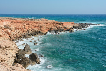 Rocky sea shore with waves and beautiful water, clear blue sky