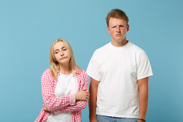 Young fun couple two friends guy girl in white pink empty blank design t-shirts posing isolated on pastel blue background studio portrait. People lifestyle concept. Mock up copy space. Looking upset.