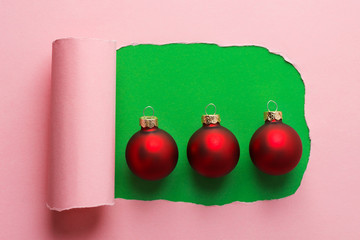 Red decorative balls on green background with torn out frame from pink backdrop. Paper art creative Christmas New years greeting card poster with copy space