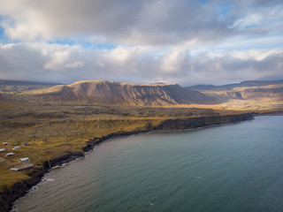 West coast sea cliffs of Snaefellsnes Peninsula on Iceland in long exposure photo. Pure blue water with high cliffs above sea. Beautiful colourful scenic view of basalt rock reef..