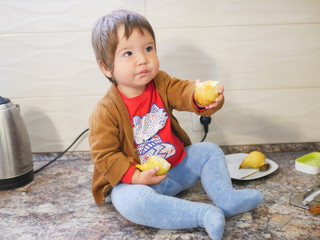 little child eats a pear. child boy eating fruits at a high stoic. in the kitchen.