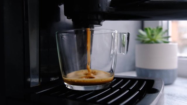 Coffee machine making espresso in glass transparent coffee cup. Hot espresso running into cup.