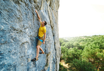 Young strong man climbing challenging route on a high vertical limestone cliff, resting and...