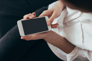 Woman hand holding white mobile phone and sitting on sofa at home.