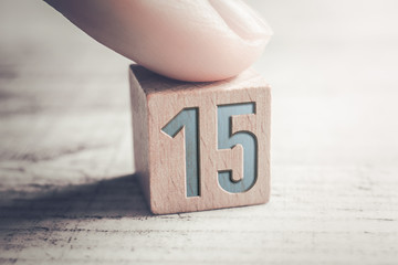 Number 15 On A Wooden Block Arranged By A Female Finger On A Table