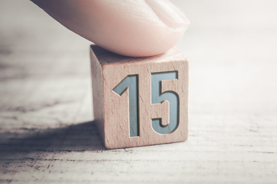 Number 15 On A Wooden Block Arranged By A Female Finger On A Table - Powered by Adobe