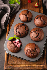 Chocolate muffins with raspberry in metal muffin baking tin, top view, vertical orientation