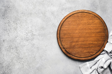Round wooden pizza board on grey concrete background and grey linen textile. Copy space for text....