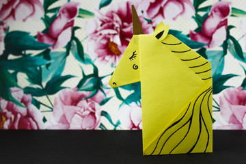 Yellow unicorn made in the origami technique on the right side of the photo on flower background.