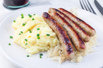 Roasted nuremberg sausages served with sour cabbage and mashed potatoes, on  white plate, horizontal