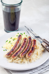 Roasted nuremberg sausages served with sour cabbage and mashed potatoes, on white plate, vertical