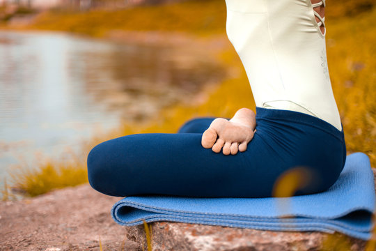 A young sports girl practices yoga on a fall yellow lawn by the river, use yoga assans posture. Meditation and unity with nature