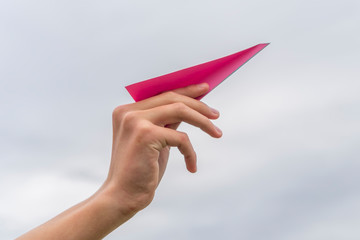 Child's hand launches a red paper airplane on a background of cloudy sky