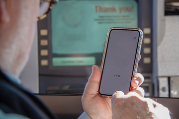 Older man attempting to use phone to complete a transaction at a drive up ATM machine - selective focus.