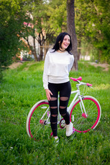 Naklejka premium girl on a red and white bike. A pretty young sexy tanned athletic girl rides in nature. cheerful and smiling brunette. good figures.