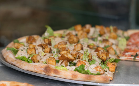 Close up photo of Caesar salad pizza ready to purchase by the slice in a new york pizzeria for customer to eat healthy option