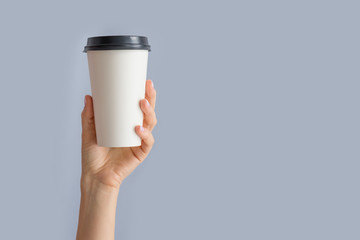 Mockup of woman hand holding up a Coffee paper cup isolated on grey background. Front view - Powered by Adobe