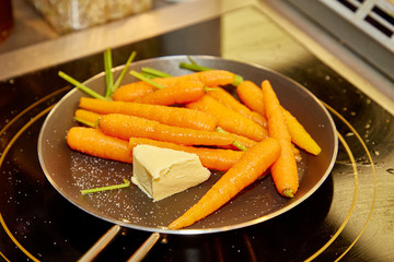 Whole young carrots are fried with butter in a skillet.