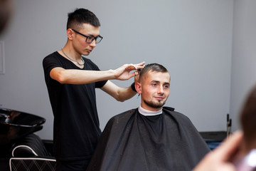 Kazakh barber gives the client a short haircut with scissors and a comb, hairdresser a student does a hairstyle