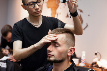 young barber kazakh works in a barbershop, handsome guy does hair styling for a client with dry gel in a hairdresser