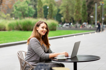 Business woman sitting in a coffee shop on the street, working at a laptop. Woman smilling and looking at camera. Germany, Frankfurt