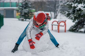 Fototapeta na wymiar A teenage girl sculpts a snowman out of snow.