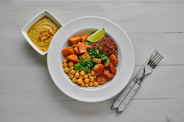 Delicious bowl with garlic grilled shrimps, sweet potato, quinoa, chickpeas, humus and lime on a white wooden table. Top view, directly above.