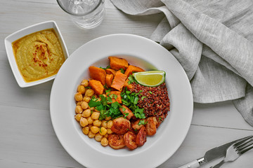 Grilled shrimps and sweet potato with black quinoa, chickpeas in a soup plate with humus and a glass of water on a white table. Top view, directly above.