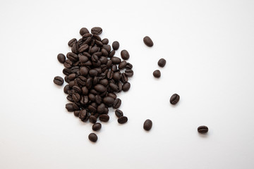 Dark roasted coffee beans on a pile on a white surface