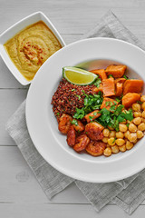 Delicious bowl with garlic grilled shrimps, sweet potato, quinoa, chickpeas, humus and lime on a white wooden table. Top view, directly above.
