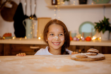 baby girl brunette is preparing gingerbread in Christmas kitchen. little girl smiling in Christmas...