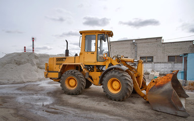 Front loader on background of storage of salt brine which using for de-icing roads. Stocks of salt mixture for treatment of icy highway. Loader and pile of salt mixture in the yard to defrost walkway